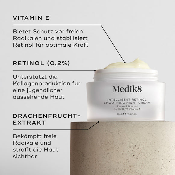 Nahaufnahme der Intelligent Retinol Smoothing Night Cream. Zu sehen ist ein weißer Tiegel mit Creme und Etiketten mit Hinweisen auf die Inhaltsstoffe. Der Hintergrund ist hell und strukturiert. Textfelder heben Vitamin E, Retinol (0,2 %) und Drachenfruchtextrakt hervor.-hover-25