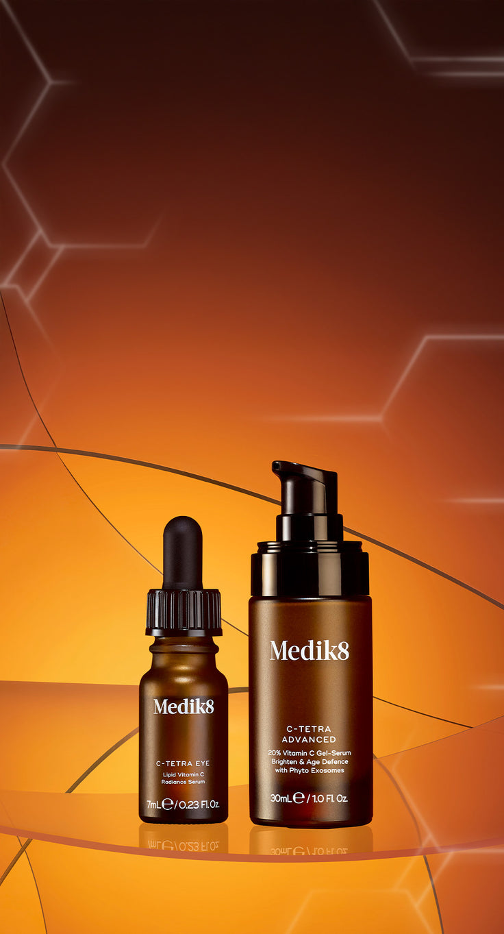 Medik8 C-Tetra Produktduo auf einem warmen, orangefarbenen Hintergrund mit abstrakten molekularen Strukturen. Zu sehen sind das C-Tetra Eye Serum (7ml) mit Pipette und das C-Tetra Advanced Serum (30ml) mit Pumpspender. Die Flaschen stehen auf einer spiegelnden Glasoberfläche.